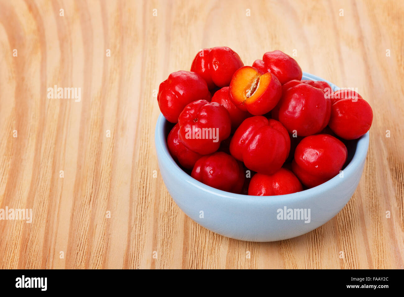 Malpighia glabra (red acerola), tropical fruit in bowl on wooden table. Selective focus Stock Photo