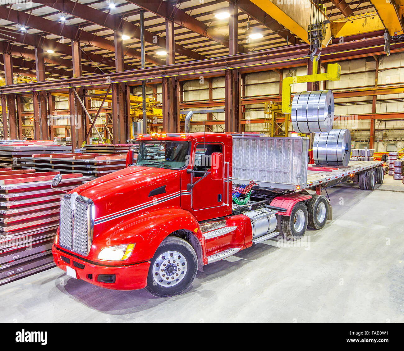 Red semi tractor trailer truck being loaded with roll formed steel coils - inside bay lit up with ceiling lights Stock Photo