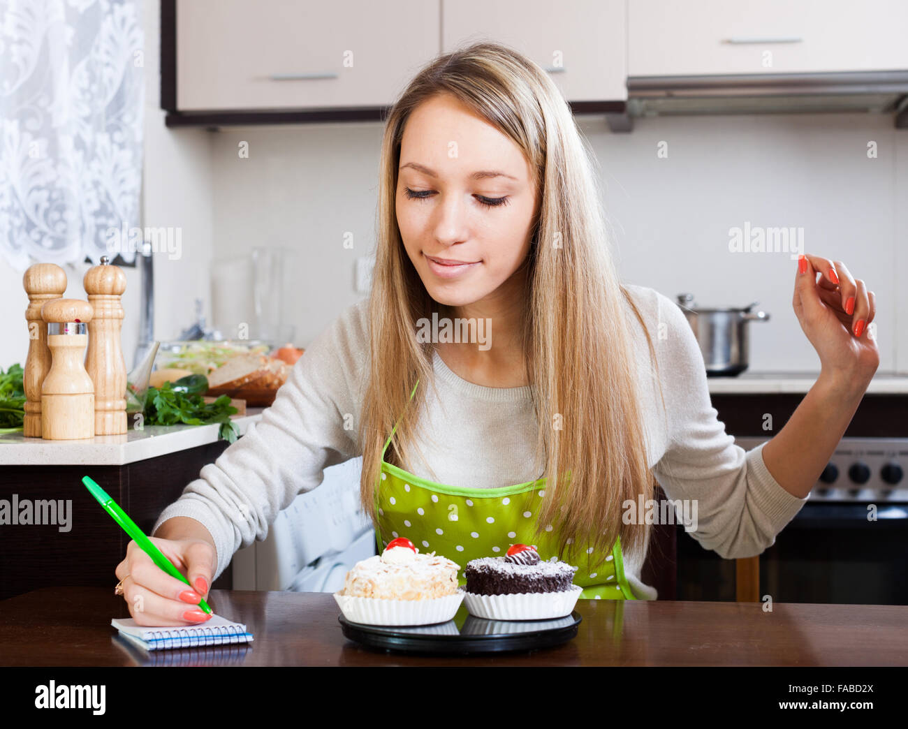 Smiling woman weighing cakes on kitchen scales at kitchen Stock Photo