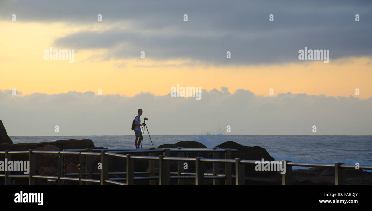 A lone photographer stands on the rocky coastline while capturing the morning light at a Sydney beach in Australia Stock Photo