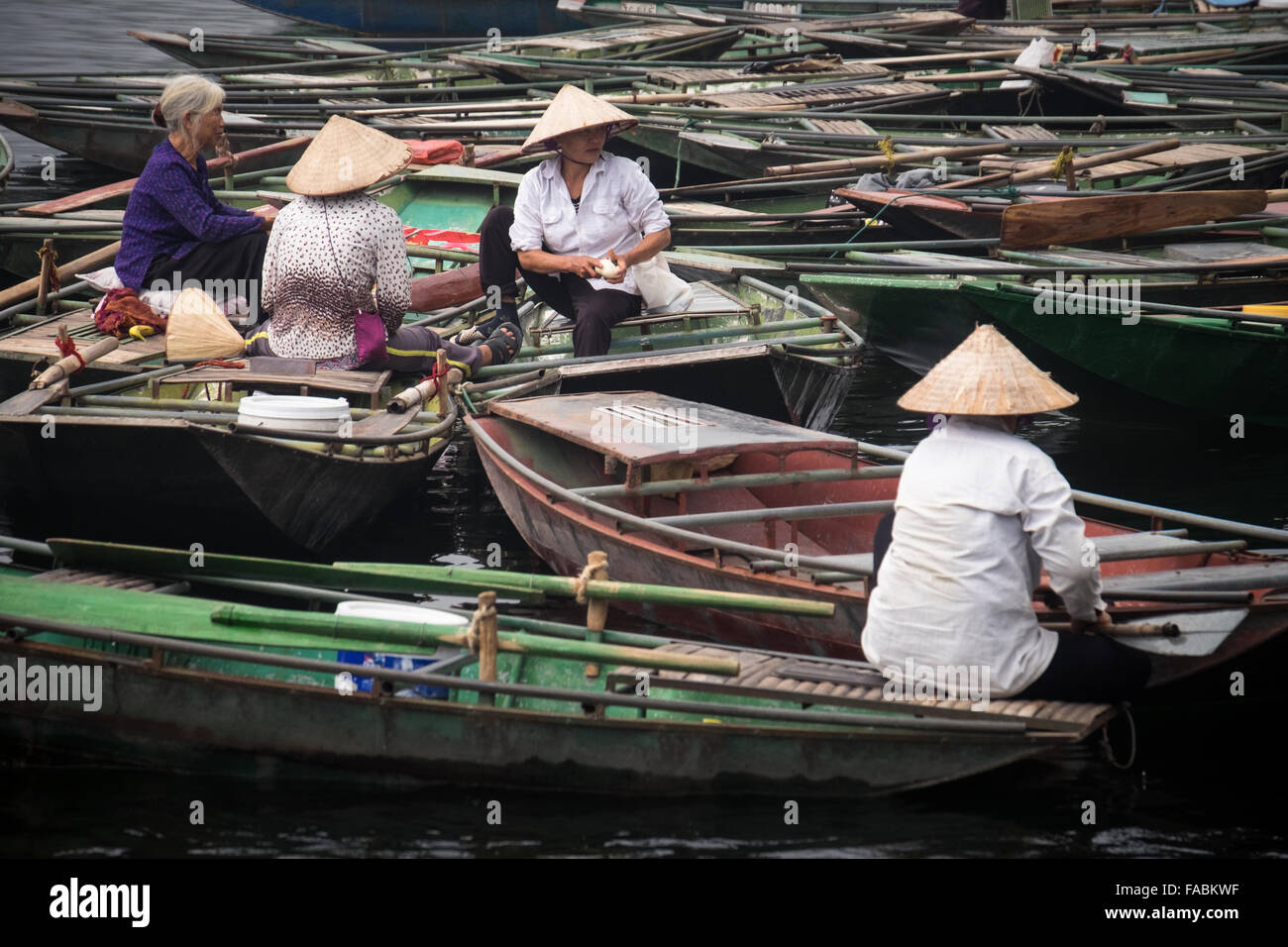 A group of women amongst the many other boats lined along the quayside at Tam Coc. Approximately 1300 people work at this location, and share the job of rowing  visitors along the 5km boat ride up the river surrounded by spectacular limestone karst scenery. Stock Photo