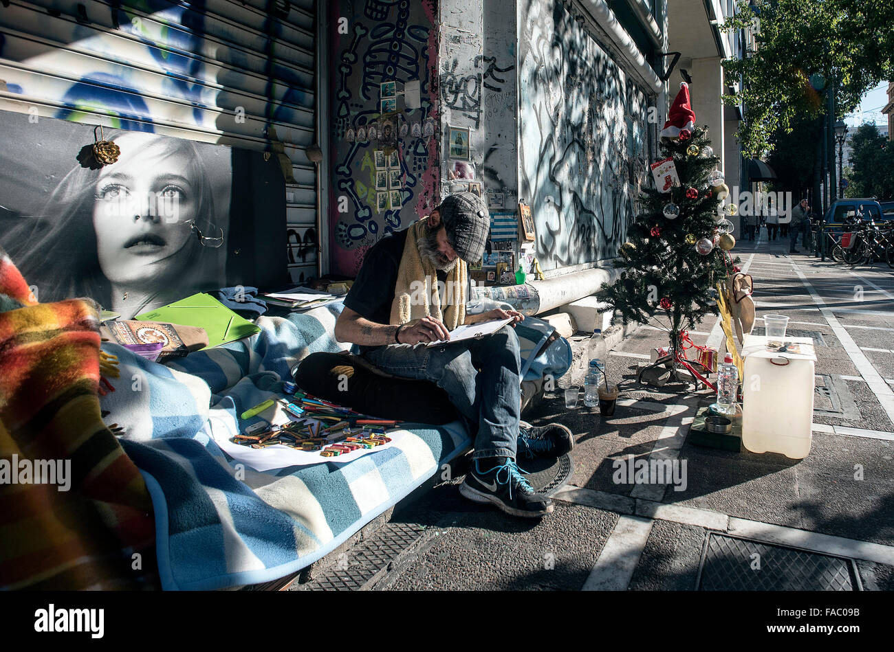 A homeless man sits next to a Christmas tree in a street in Athens