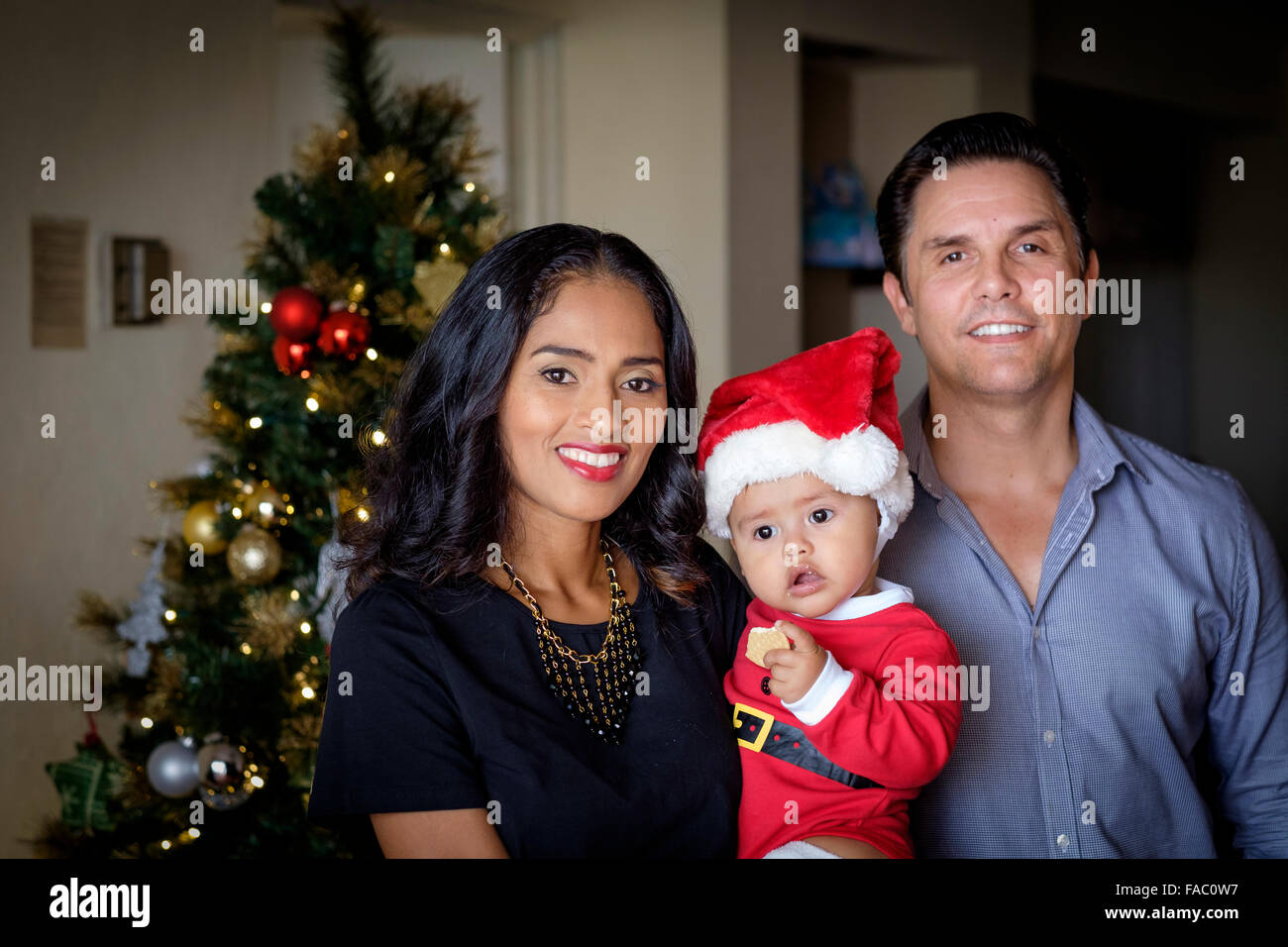 Christmas portrait of a multi-ethnic family. Mother is of hispanic, while father is of ccaucasian ethnicity. They're holding the Stock Photo
