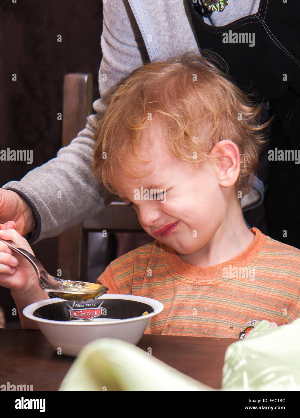 A young , blond hair boy is eating soup on his own . Stock Photo