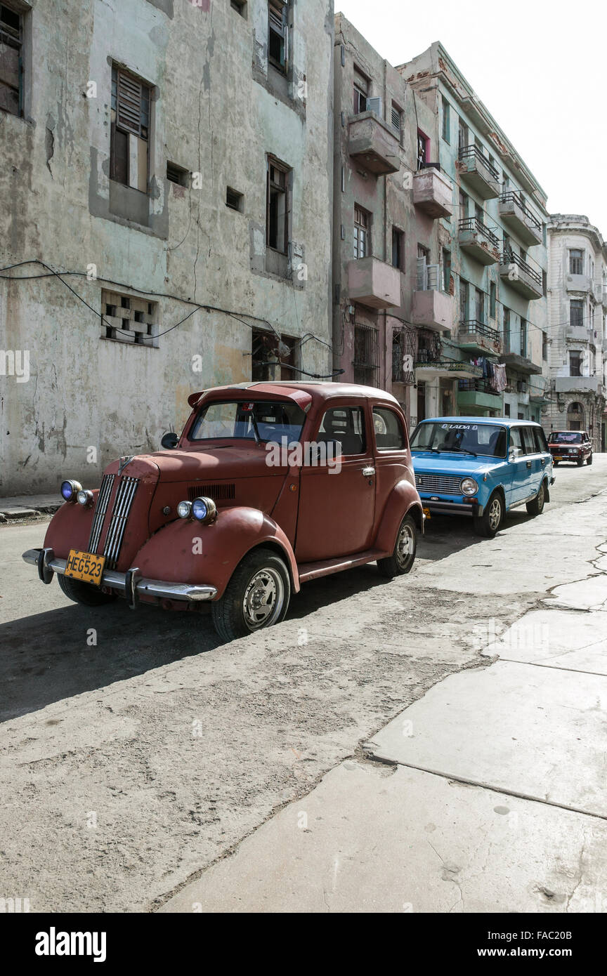 A red vintage automobile parked along a stone curb on a street in Havana Cuba with a newer blue car parked behind it. Stock Photo