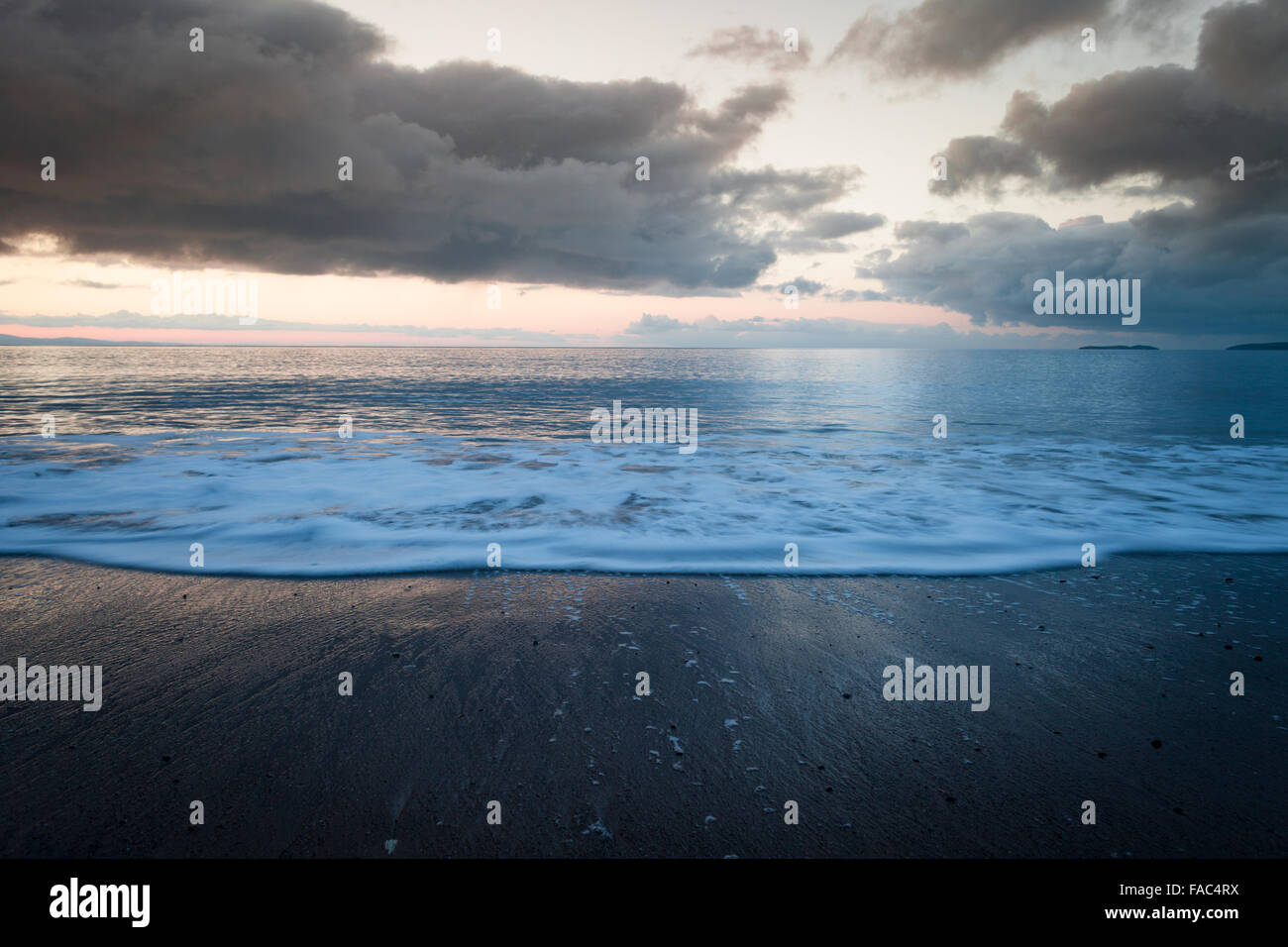 Rainy Sunrise Clouds over Coastal Beach with Wave in Motion Stock Photo
