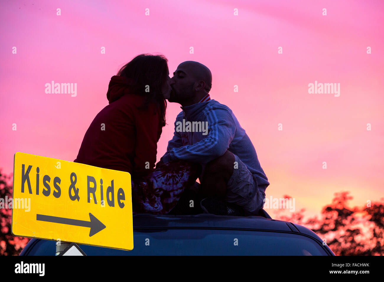 A couple sat on a car roof watching a glorious sunset over Lydford, Dartmoor, Devon, UK with a funny sign. Stock Photo
