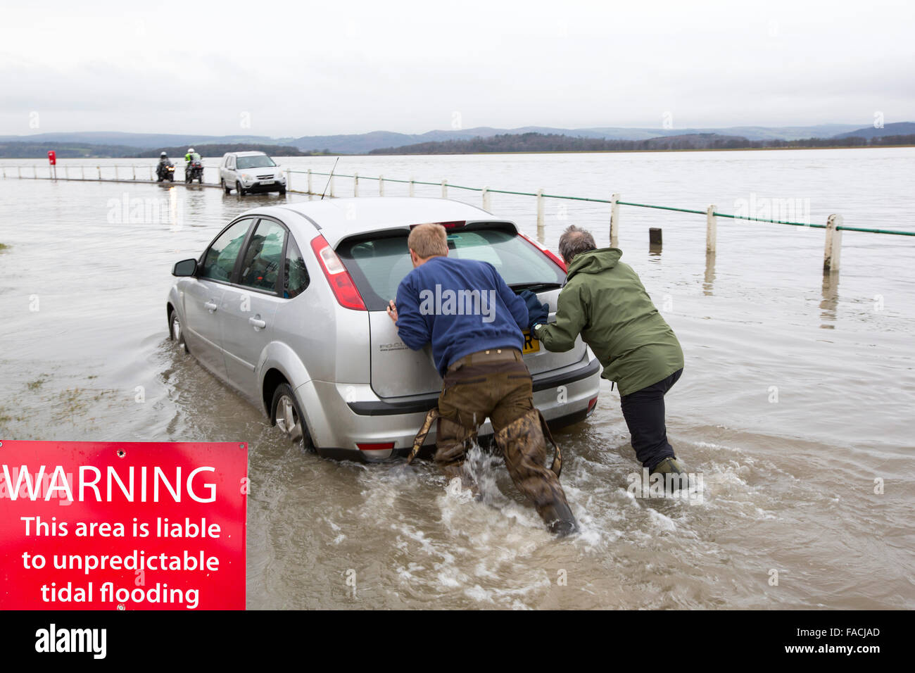 A motorist stuck in flood waters on the road at Storth on the Kent Estuary in Cumbria, UK, during the January 2014 storm surge and high tides, is pushed out by two helpers. Stock Photo