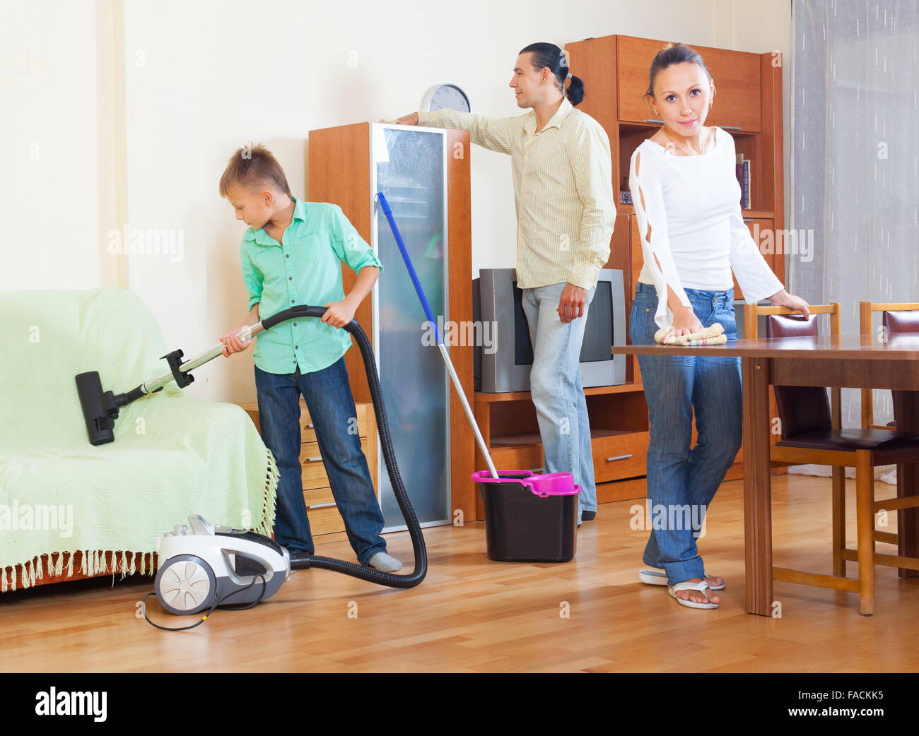 Happy family of three cleaning with vacuum cleaner in home Stock Photo
