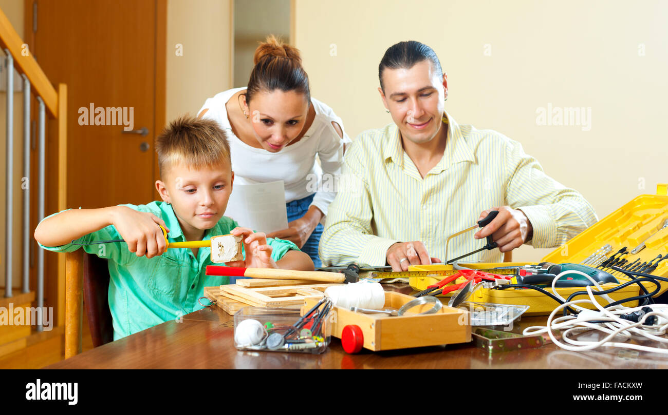 Son with father doing something with working tools, happy woman watching them at home Stock Photo