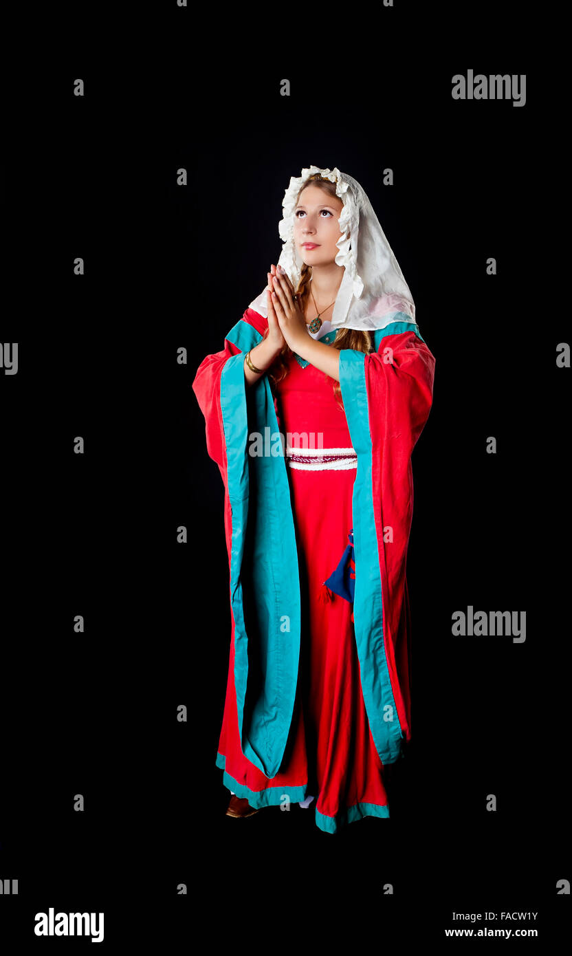Studio shot of beautiful girl dressed in medieval costume dress and head scarf praying over black background Stock Photo
