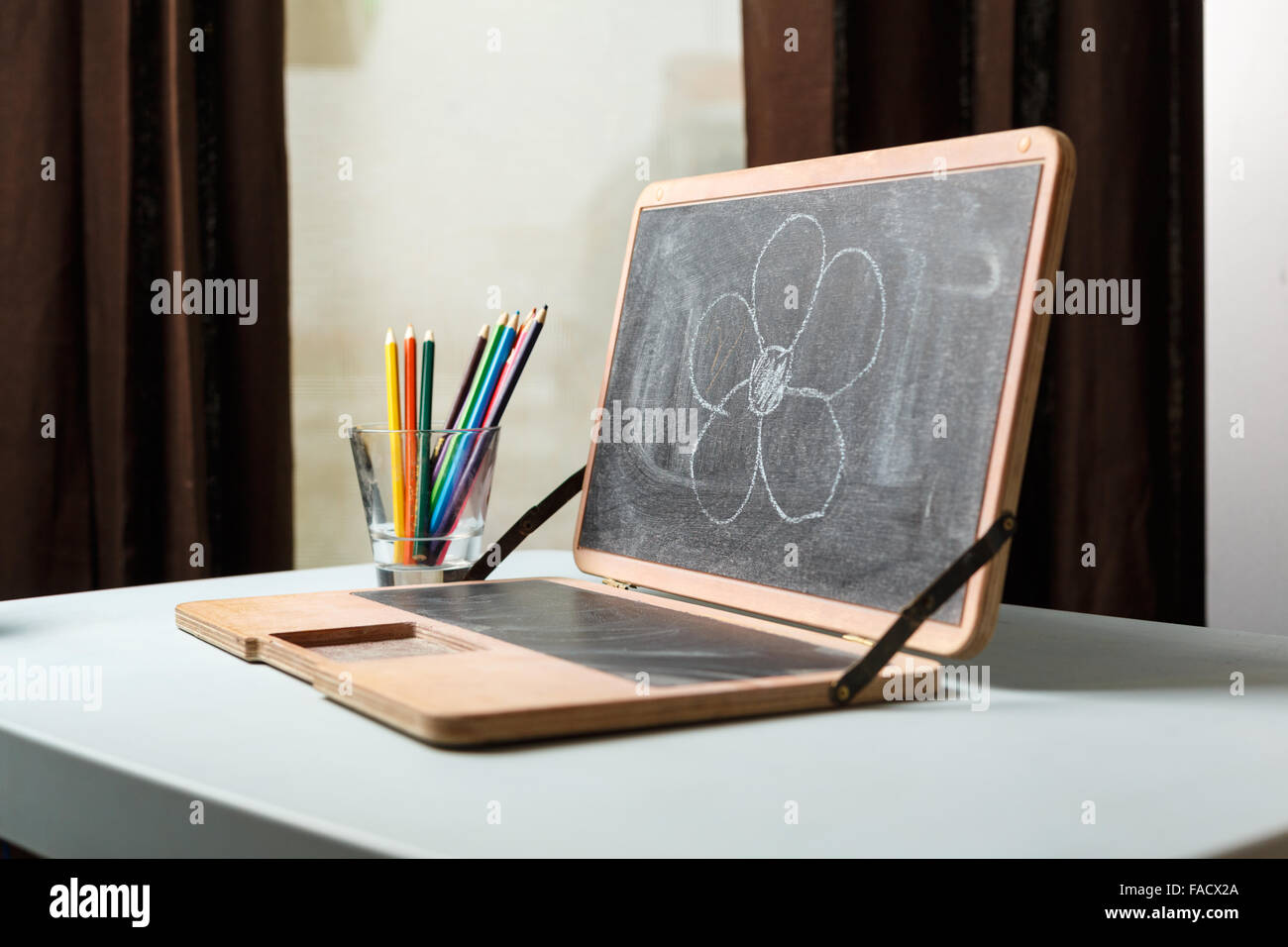 Chalkboard in a form of a laptop with color chalks and penс ils in a glass with flower painted on a board Stock Photo