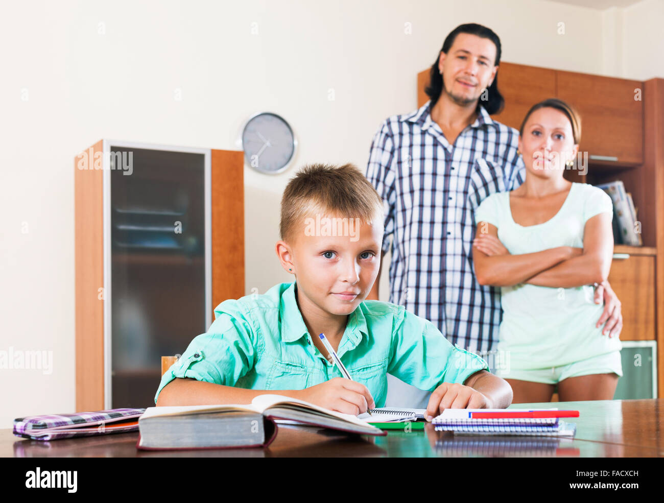Smiling couple watching on teenager son doing homework in home interior Stock Photo