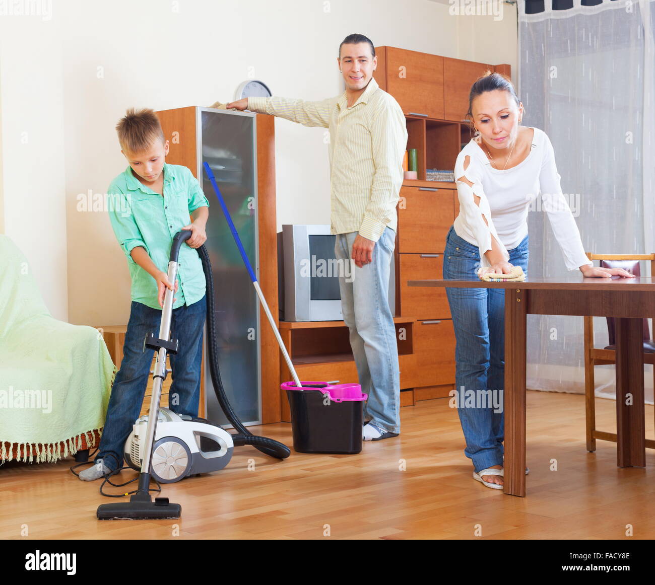 Happy family of three with teenager doing housework together in home Stock Photo
