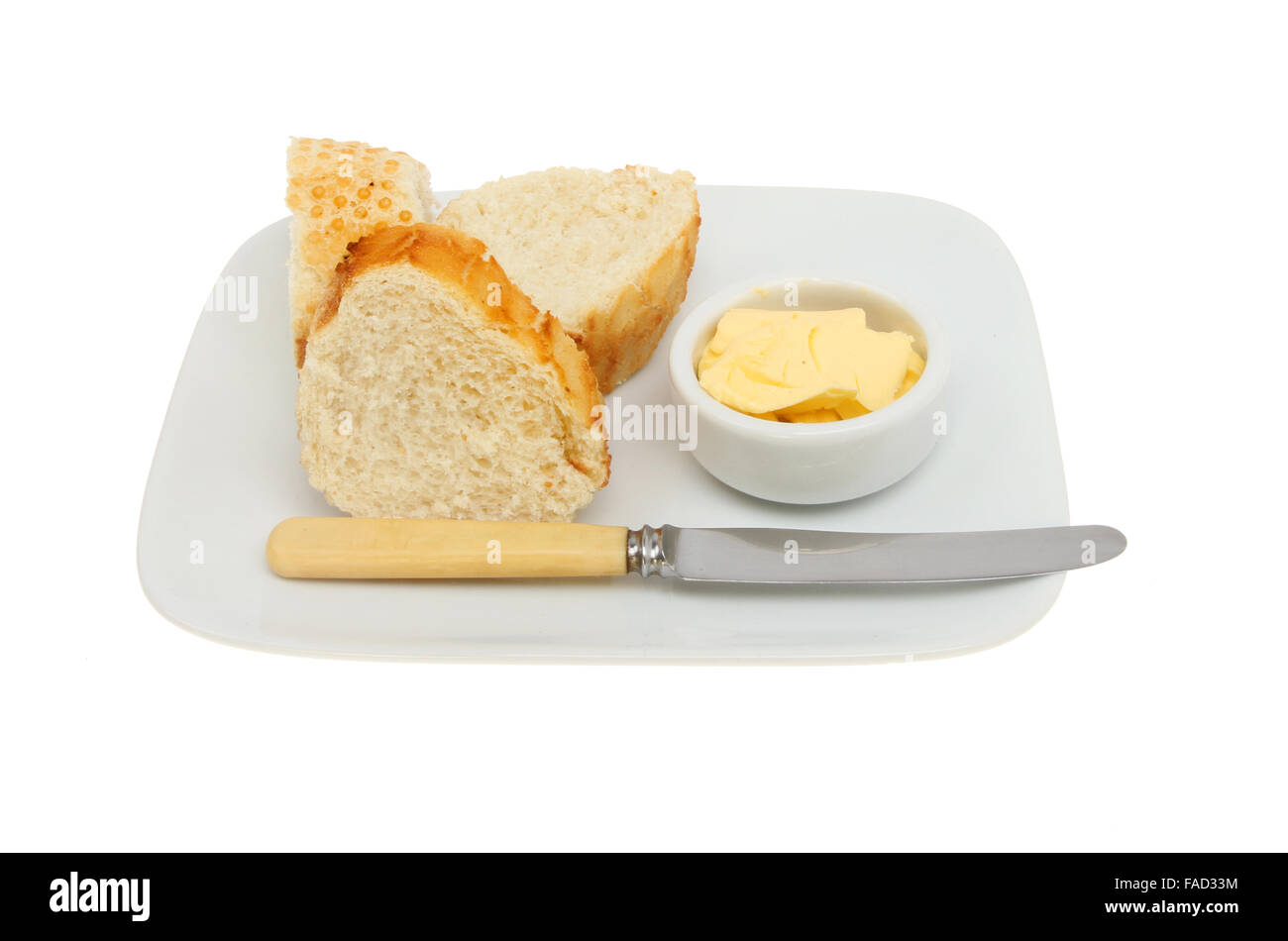 Crusty bread with butter in a ramekin and a knife on a plate isolated against white Stock Photo