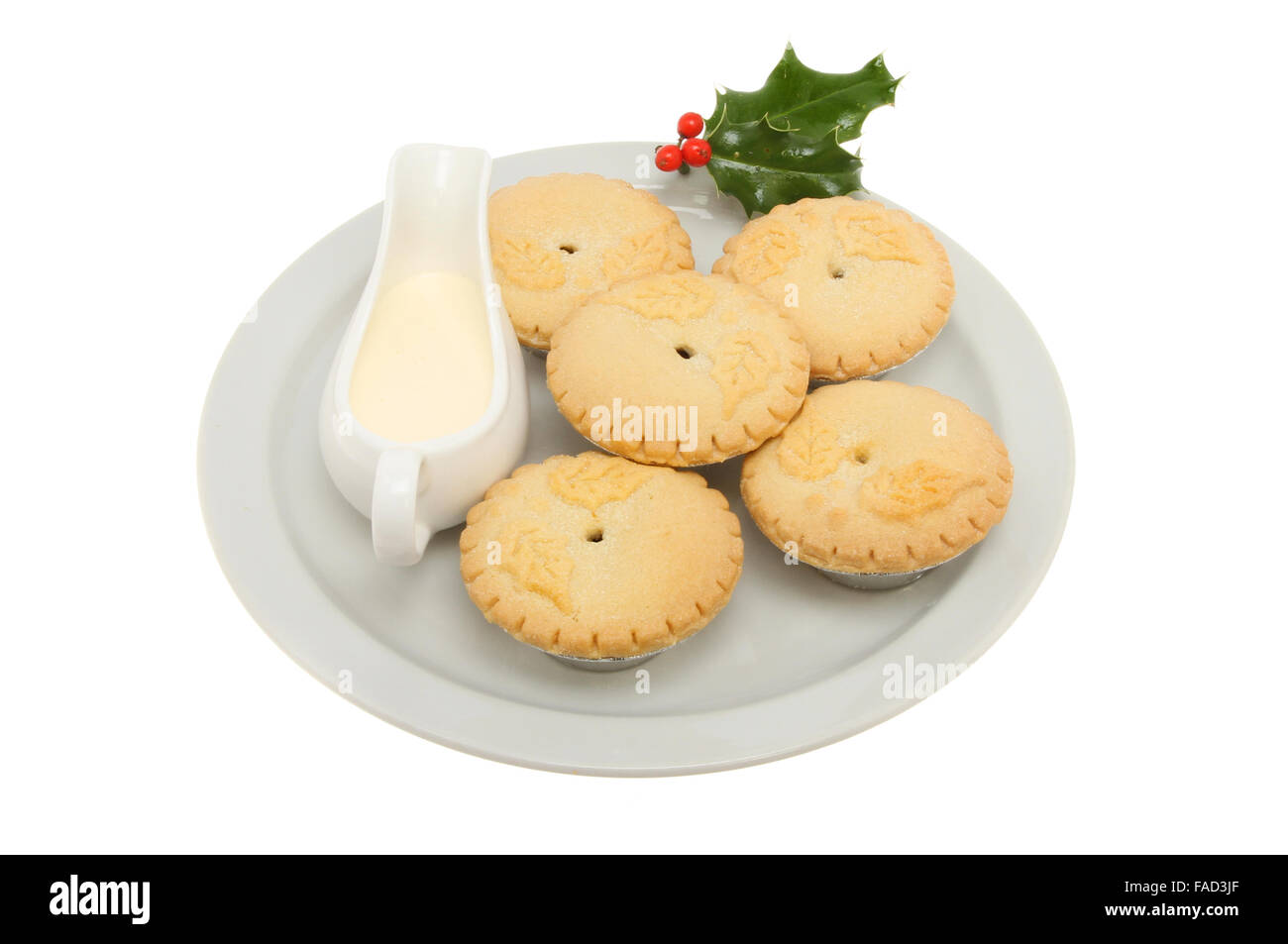 Mince pies on a plate with a jug of cream and a sprig of holly isolated ...