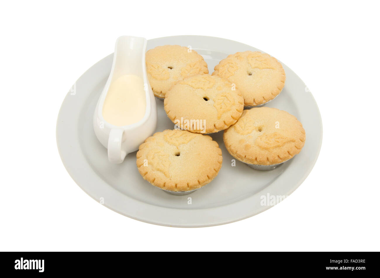 Holly decorated mince pies on a plate with a jug of cream isolated ...