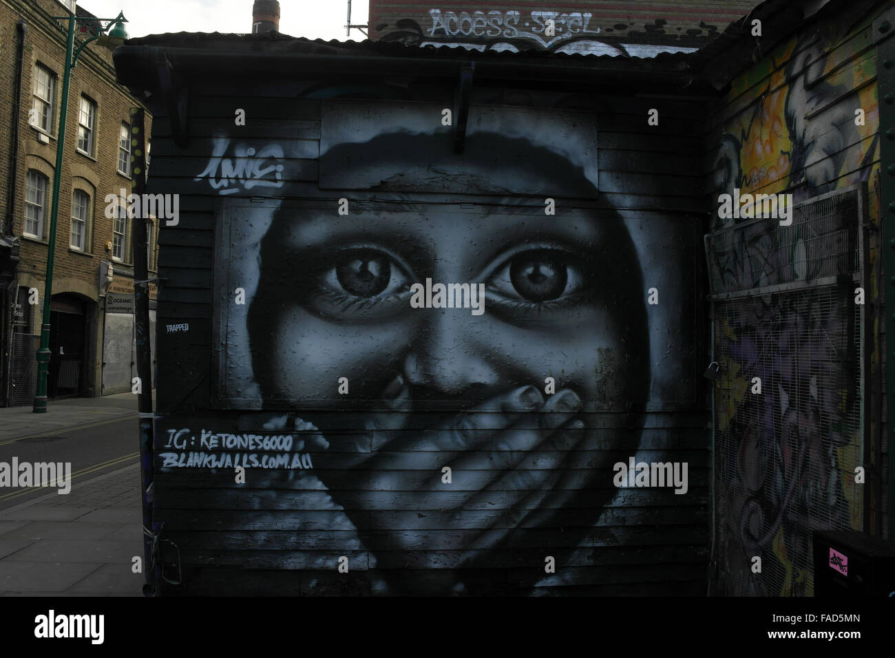 Grey sky view Ketones 6000 monochrome face with hand over mouth, shop wall, Brick Lane at Pedley Street, London, E1, UK Stock Photo