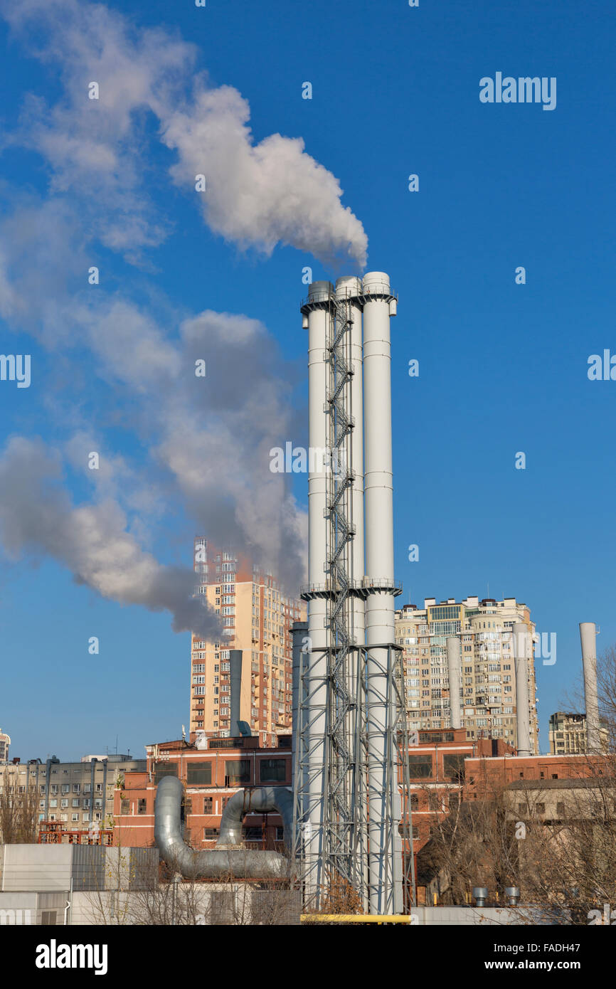Pipes of a thermal power plant with a smoke against a city landscape Stock Photo