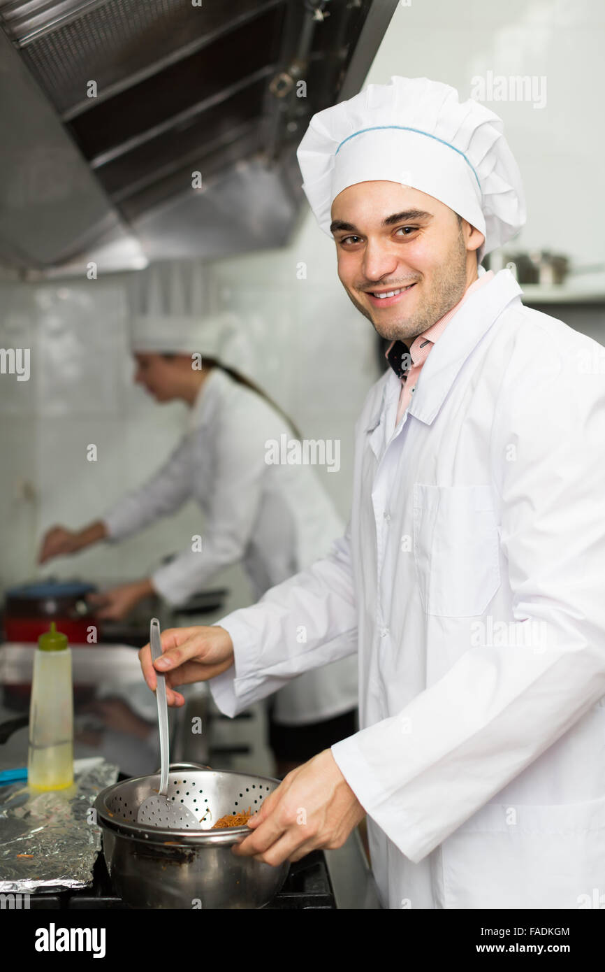 Smiling chef with assistant cooking at professional kitchen in the ...