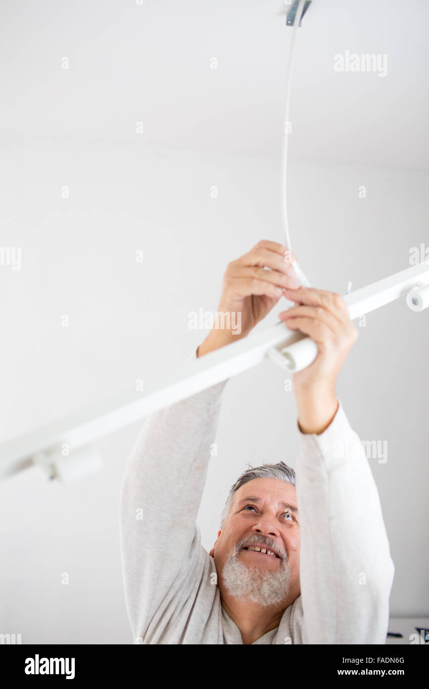 Senior man installing a ceiling light in a freshly renovated appartment ...
