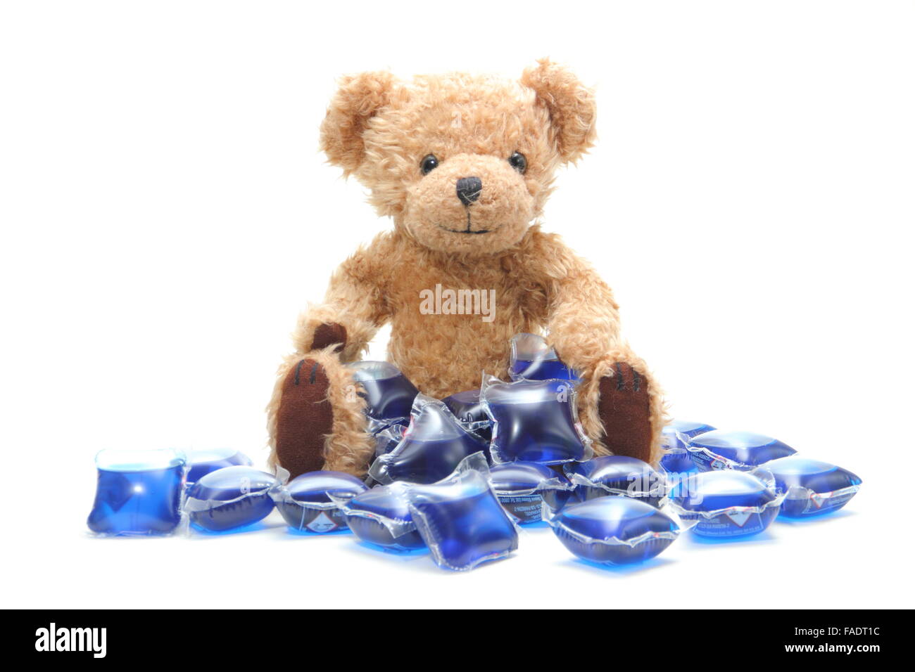 Liquid laundry detergent capsules surround a child's teddy bear - UK Stock Photo