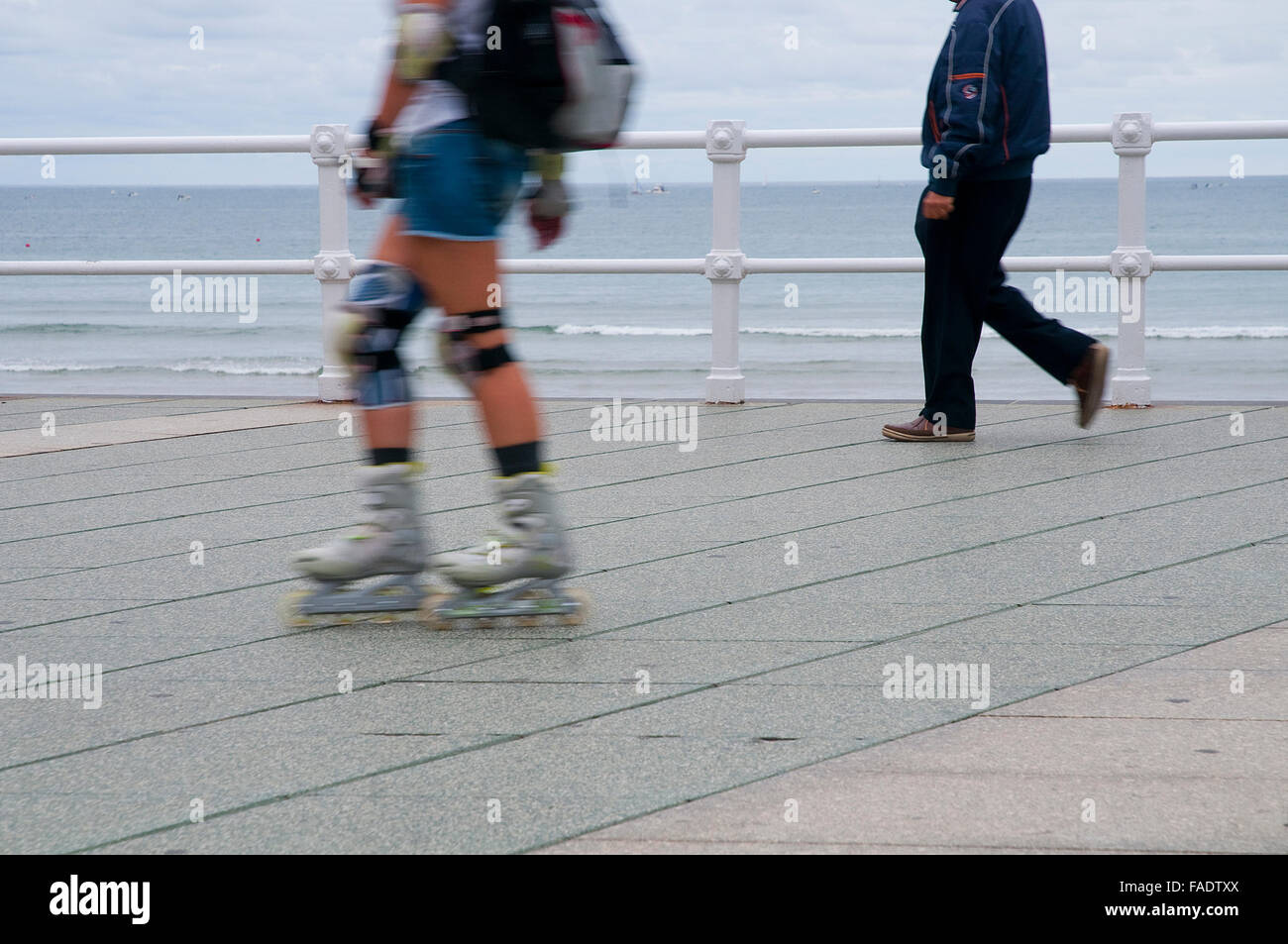Two people walking and skating in the promenade. Gijon, Asturias, Spain. Stock Photo