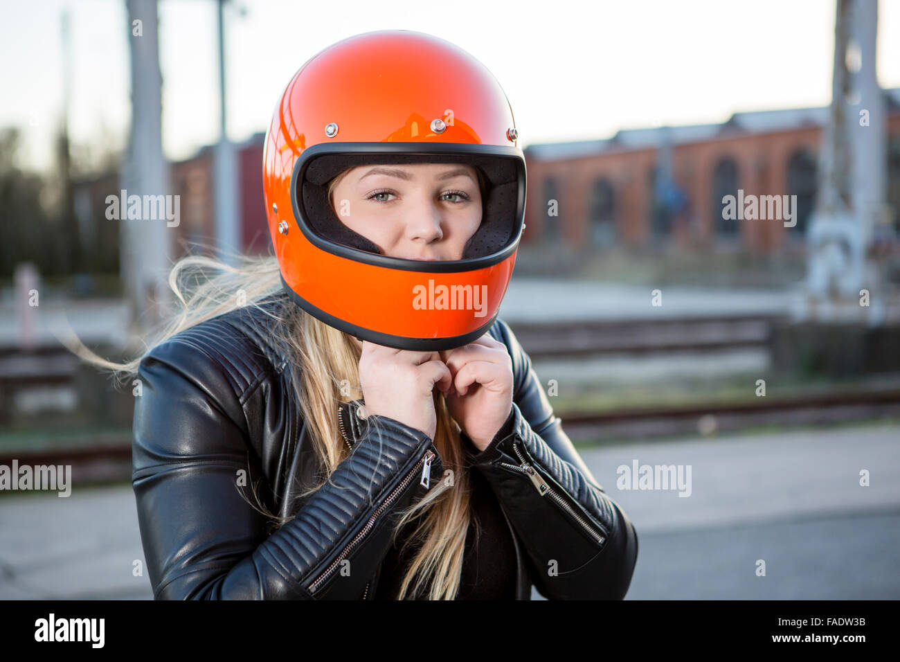 Cute girl with blond hair with orange motorcycle helmet. Outdoor, urban scene. Stock Photo