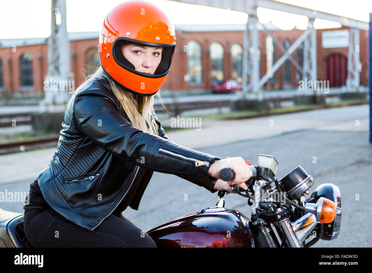 Cute girl with blond hair with orange motorcycle helmet. Outdoor, urban scene. Stock Photo