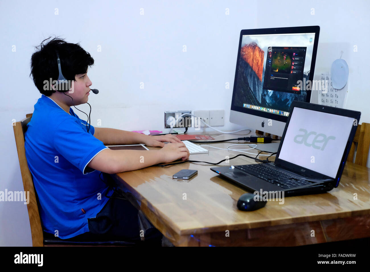 young boy sat playing games on computer surrounded by electronic gadgets england uk Stock Photo