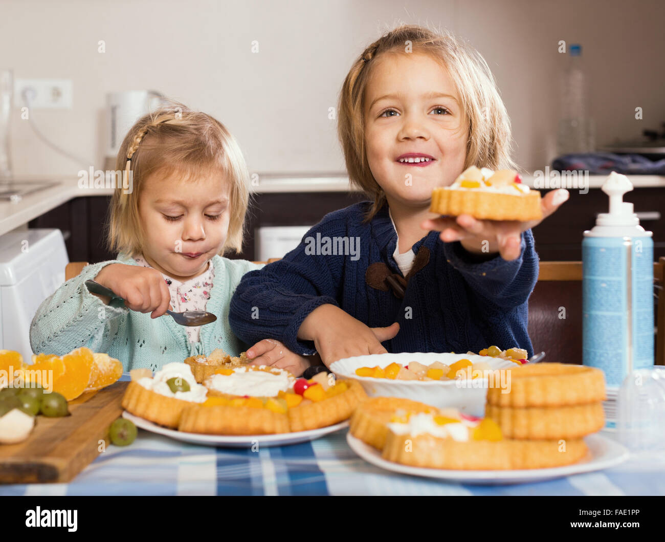 Happy cute little girls eating cream desserts at home kitchen Stock