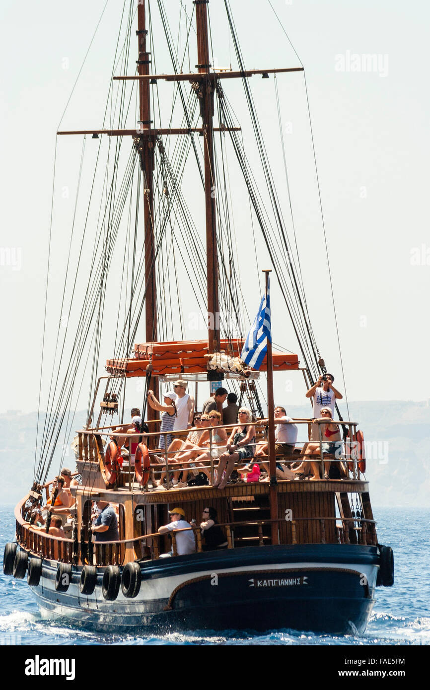 Cyclades, Santorini. Packed tourist Greek sail and motor tourist excursion boat sailing away in