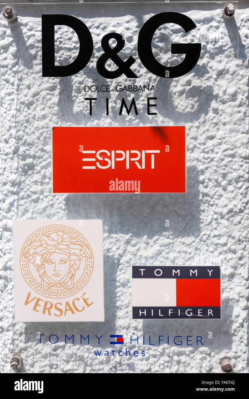 Greece. Plastic transparent sign with various band logs D&G, Versace and "Tommy Hilfiger". Background whitewashed textured wall Stock Photo -