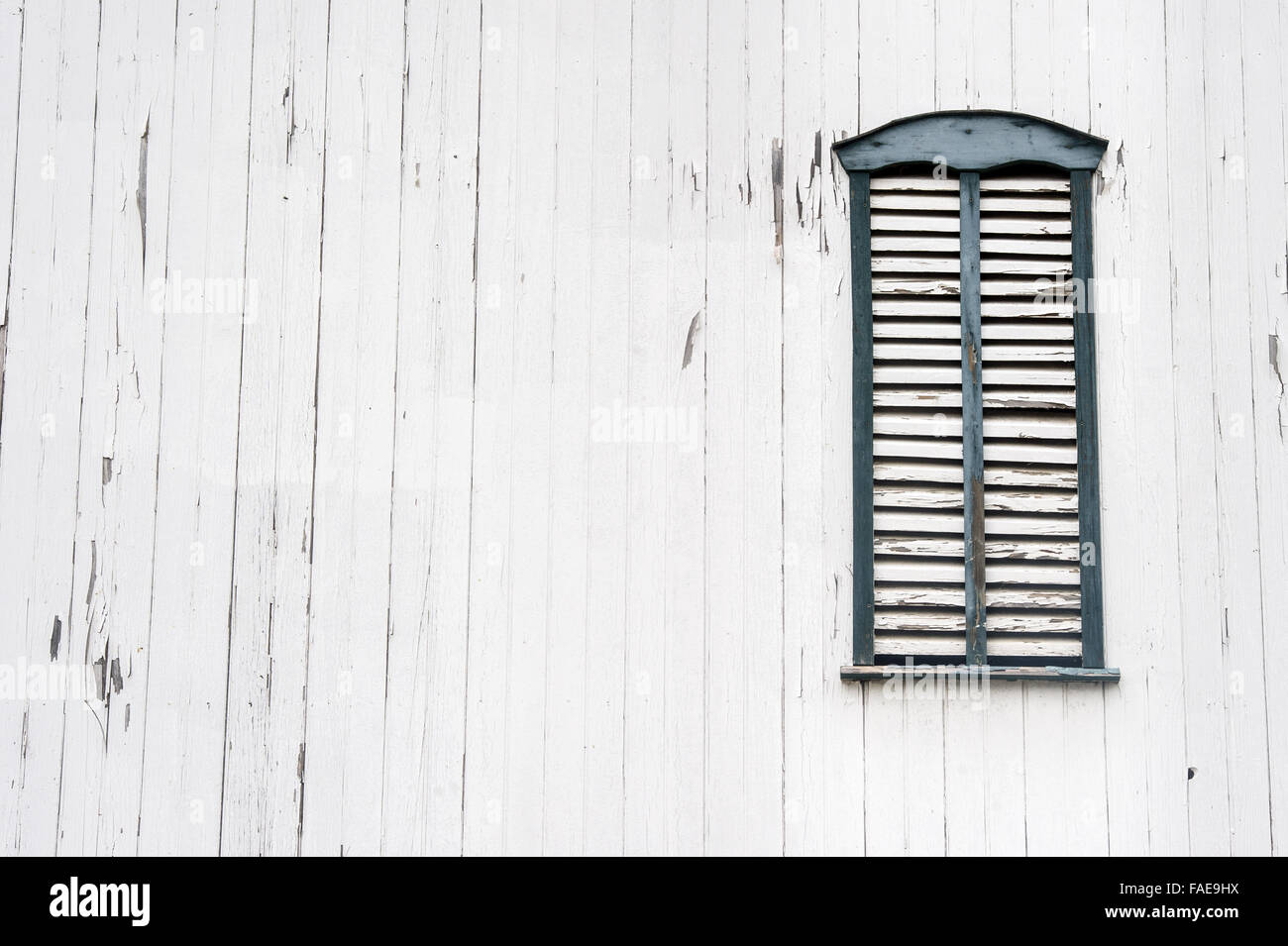 Window with closed shutters in the side of an old white barn Stock Photo