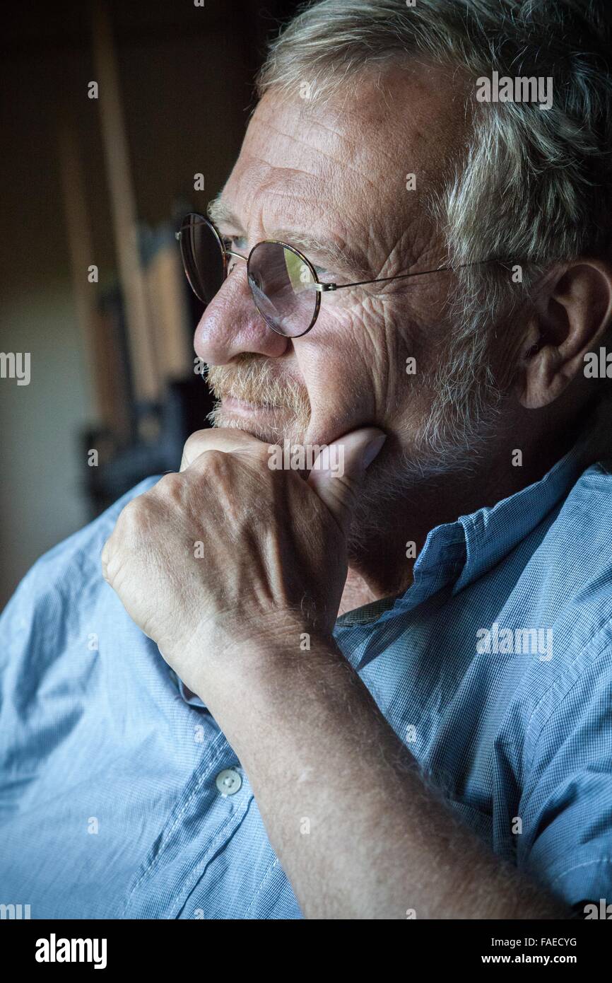Gentleman sits and ponders, portrait of an older Caucasian man, hand on chin appears to be looking out the window Stock Photo