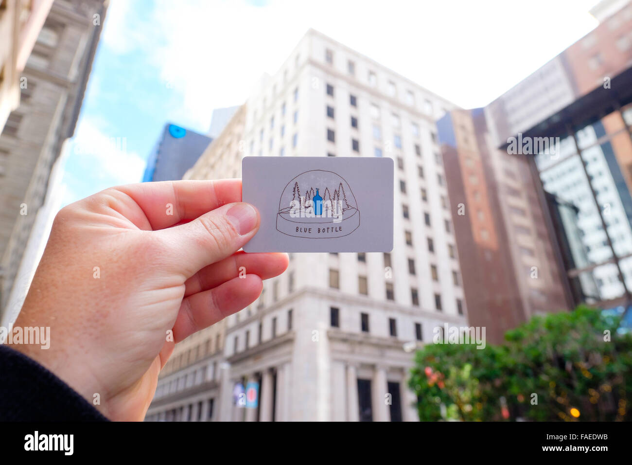 SAN FRANCISCO, CA - DECEMBER 13, 2015: Blue Bottle Coffee gift card held up in hand with downtown buildings in the background. Stock Photo