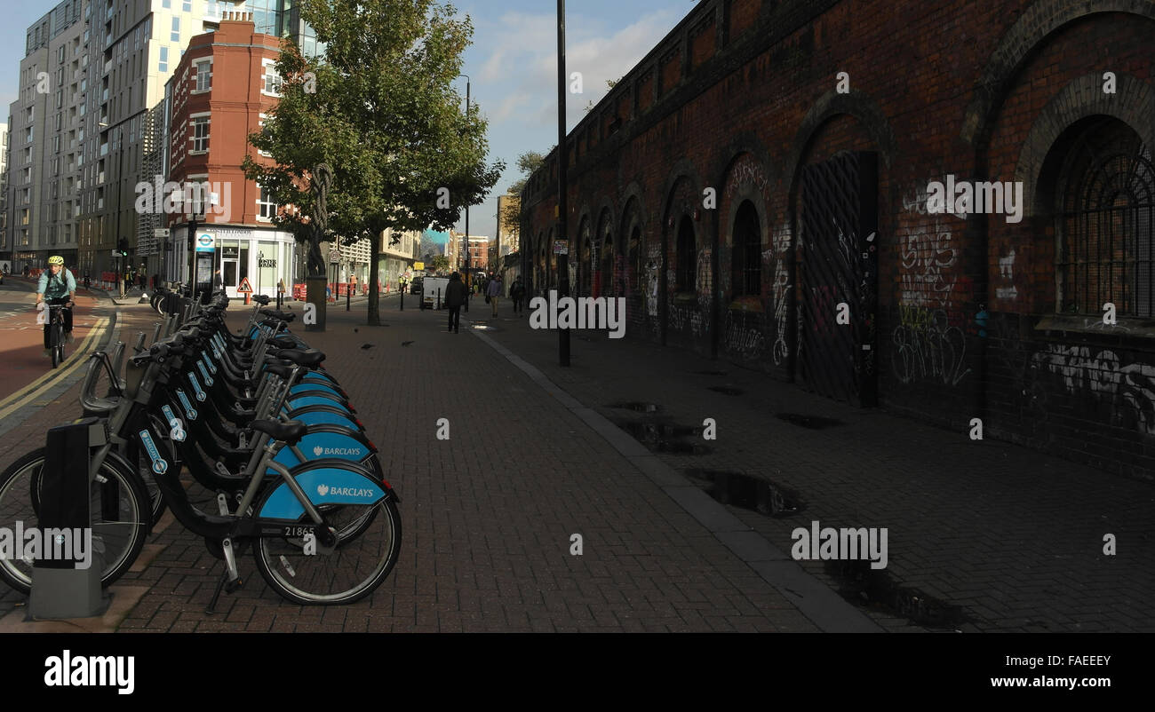 Barclays cycle hire docking station by old railway wall with graffiti scrawl, Bethnal Green Road to Sclater Street, London, UK Stock Photo