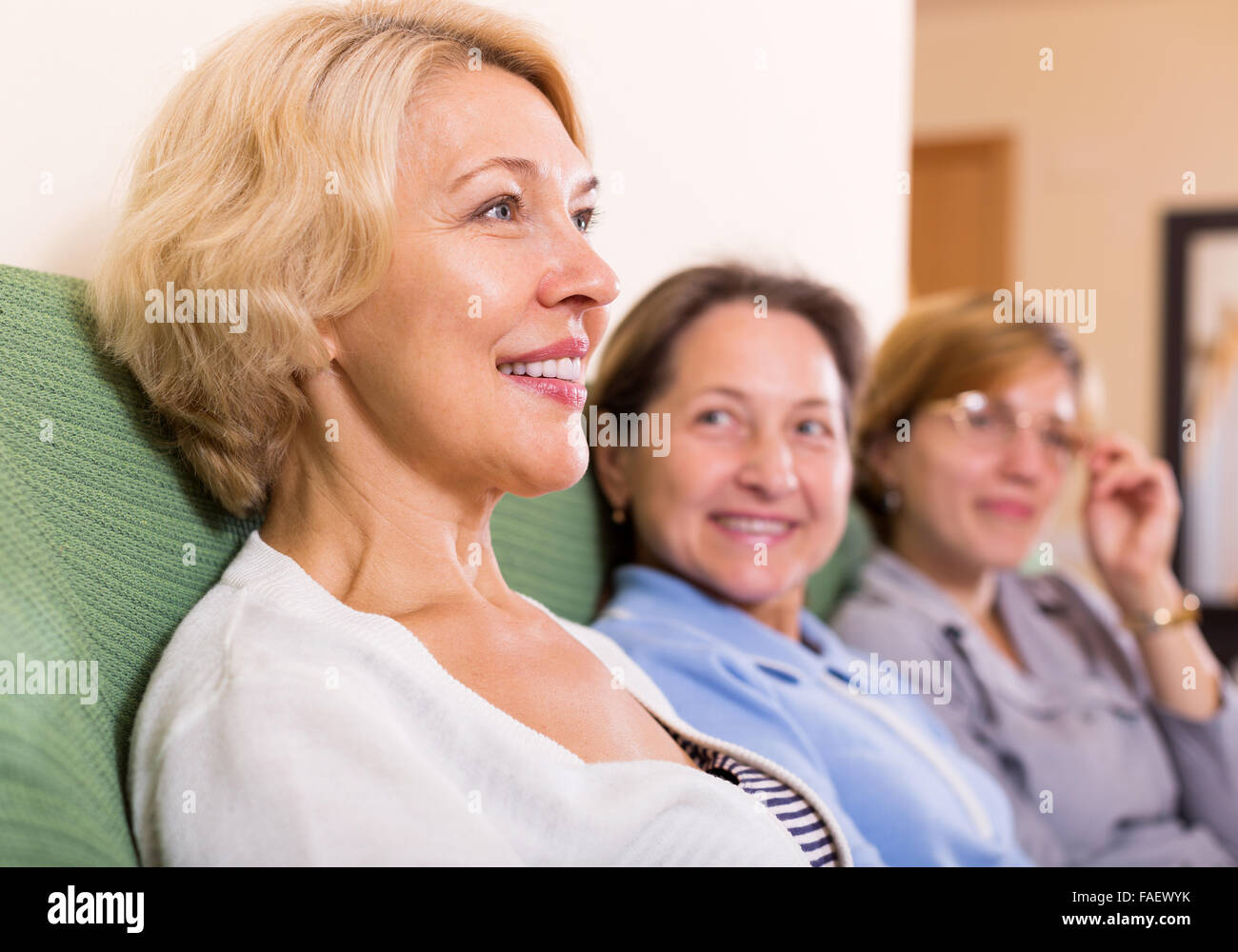 three smiling mature women at home interior sit on the couch Stock ...