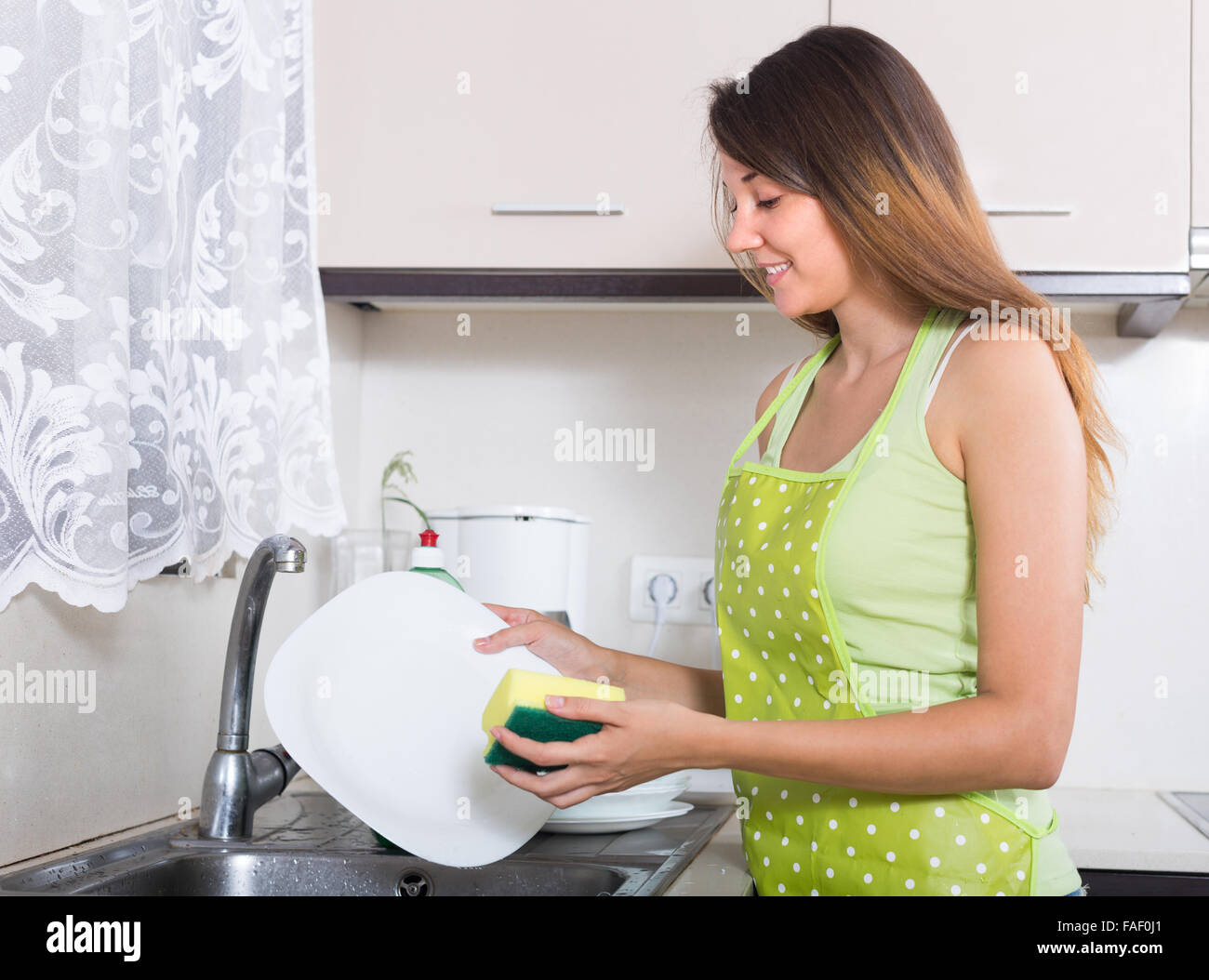 https://c8.alamy.com/comp/FAF0J1/young-smiling-woman-in-apron-washing-kitchenware-in-the-kitchen-FAF0J1.jpg