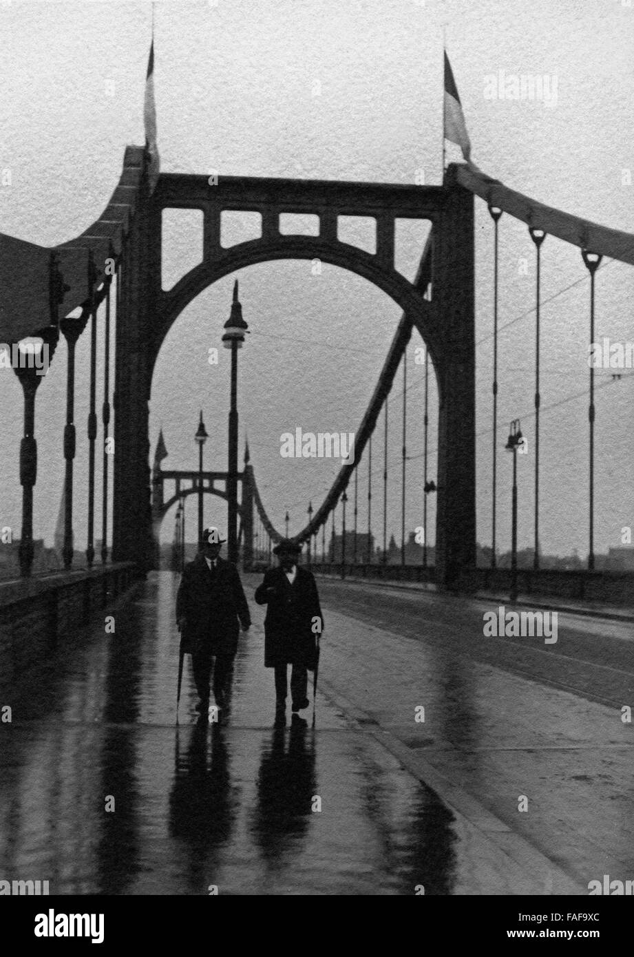 Zwei Männer bei einem Spaziergang auf der regennassen Hindenburgbrücke in Köln, Deutschland 1920er Jahre. Two men strolling over Hindenburgbruecke bridge at a rainy day at Cologne, Germany 1920s. Stock Photo