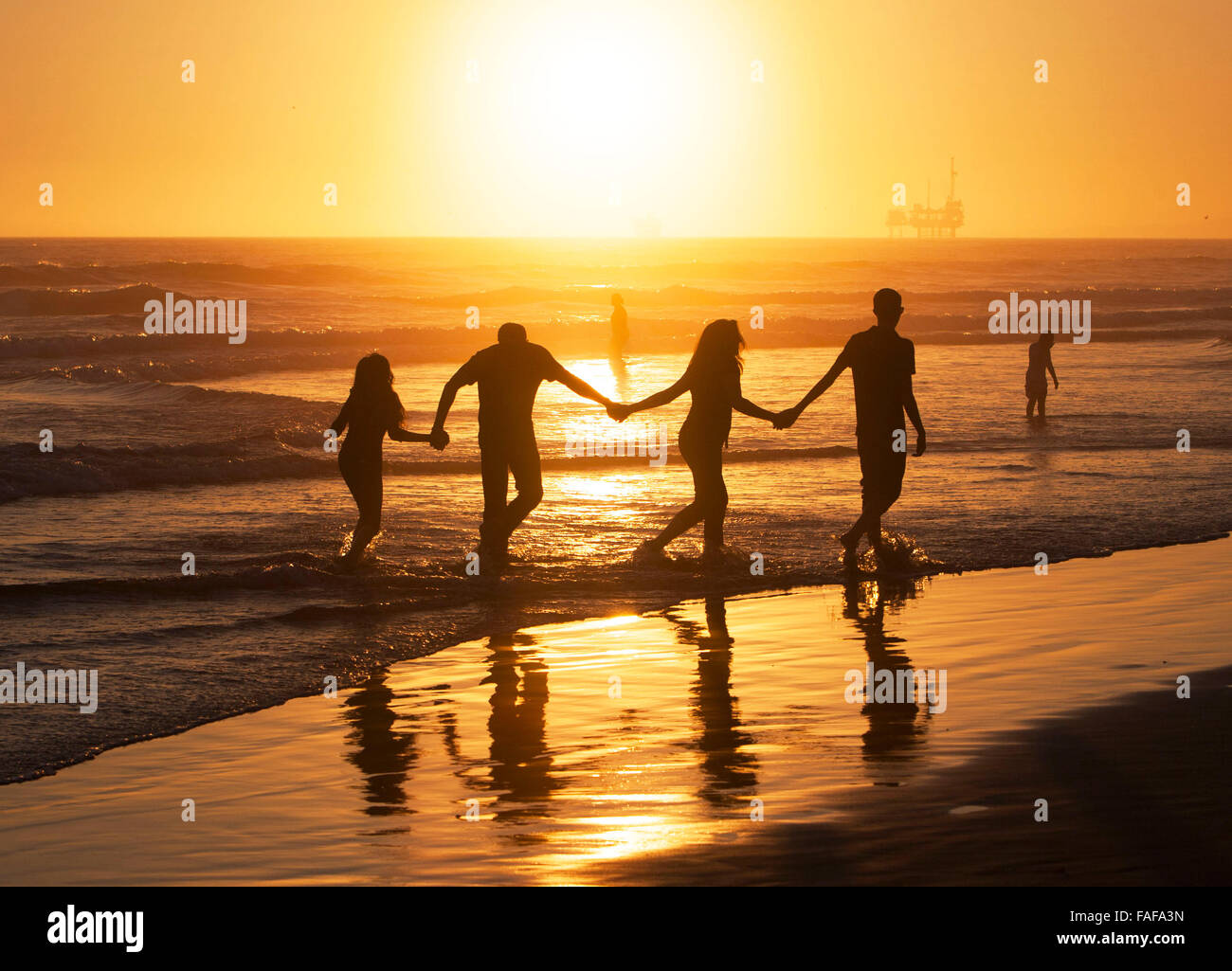 Silhouette of family friends holding hands on the beach at sunset Stock Photo