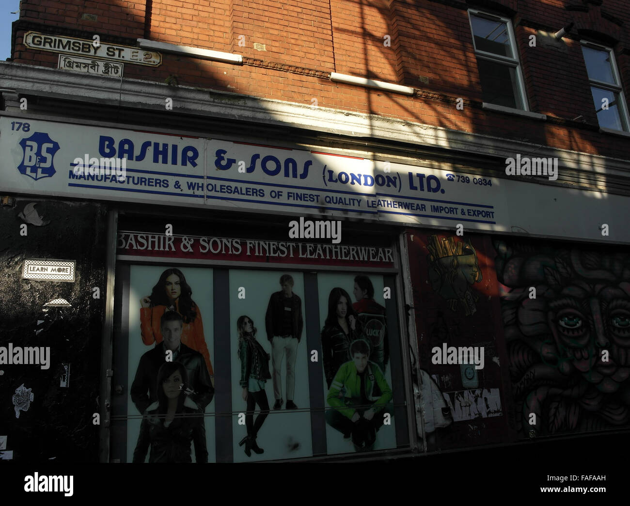 Sun shade view Bashir and Sons Leatherwear Shop, next to abstract face image, Grimsby Street at Brick Lane, London, E2, UK Stock Photo