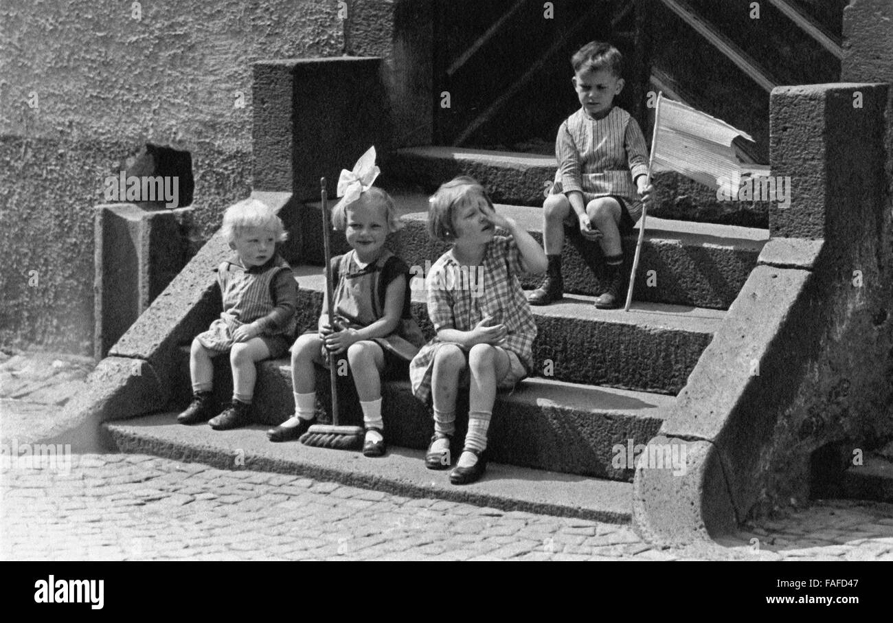 Kinder sitzen im Sonnenschein auf einer Treppe, Deutschland 1920er Jahre. Children sitting on stairs to an house entrance in the sun, Germany 1920s. Stock Photo