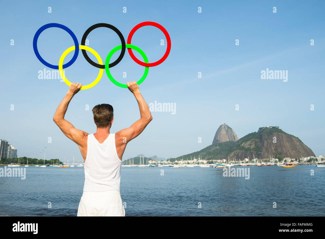 RIO DE JANEIRO, BRAZIL - NOVEMBER 10, 2015: Athlete holds Olympic rings near Sugarloaf Mountain on the shore of Botafogo Beach. Stock Photo
