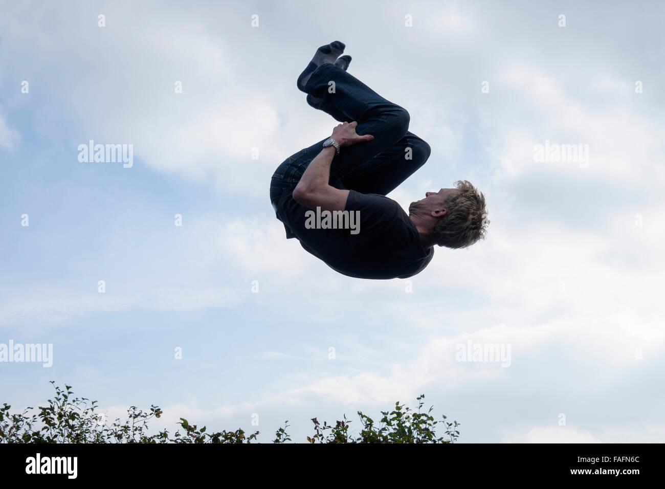 Man doing a somersault in mid air above trees against the sky. England, UK, Britain Stock Photo