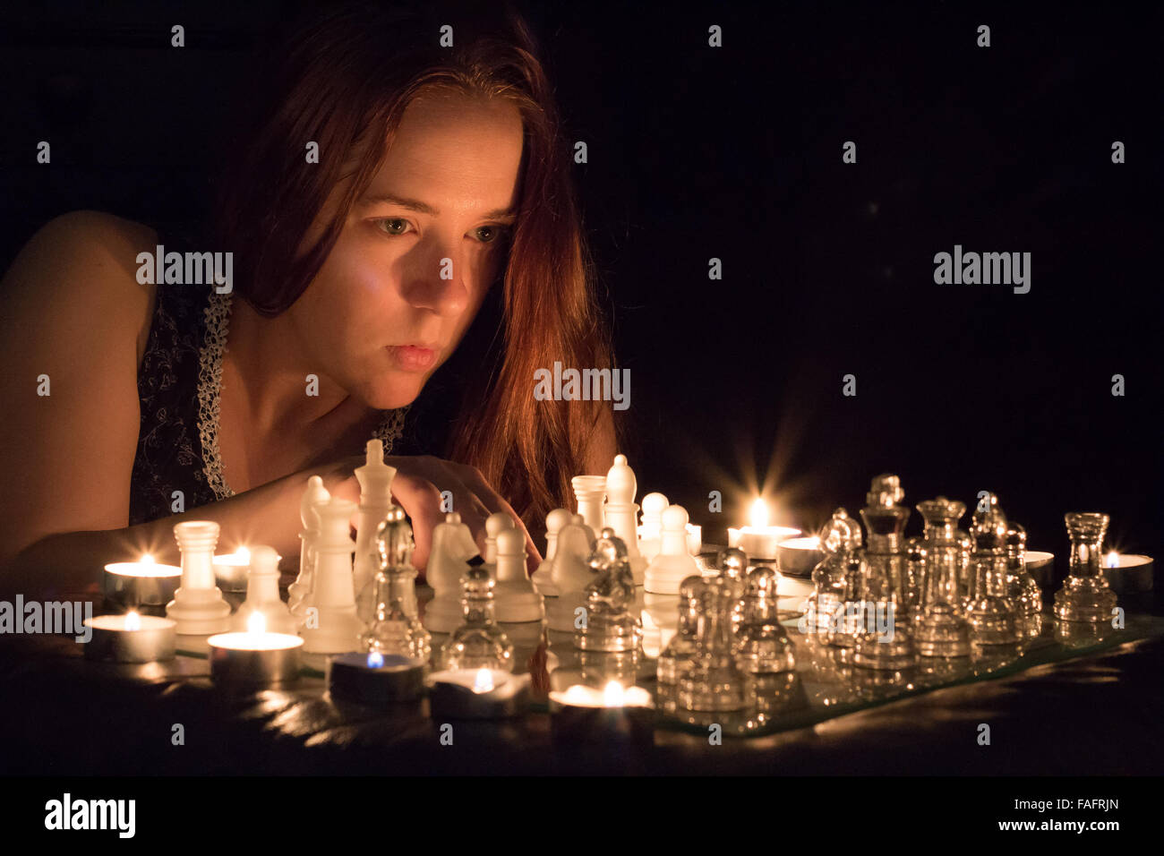 Woman playing chess by candlelight. Stock Photo