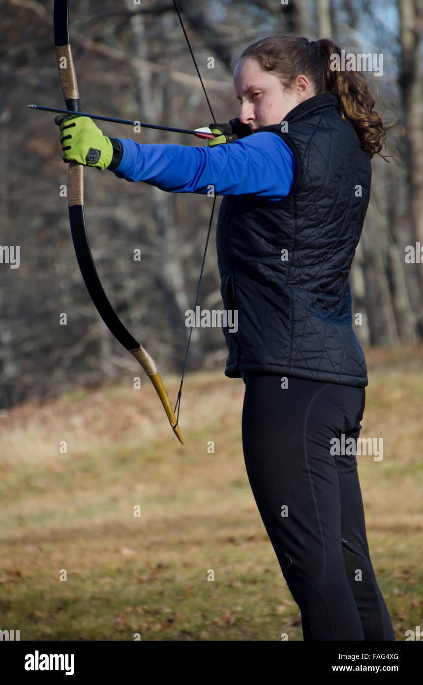 Young woman pulls back the bow. Practicing archery. Fall, Maine, USA Stock Photo
