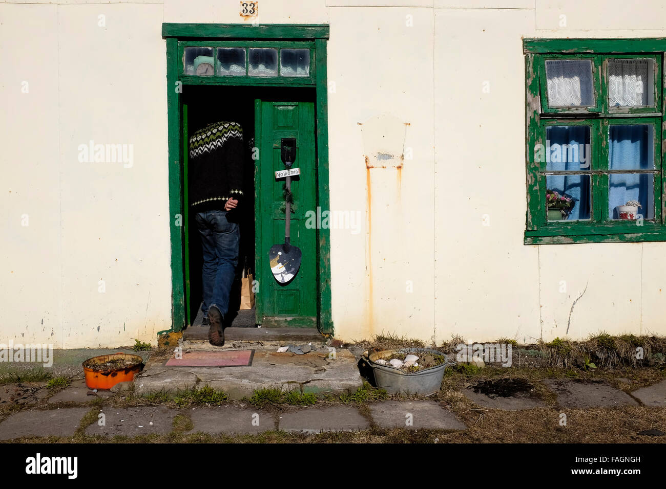 A man walks through the door of a house in Isafjordur against dramatic mountains behind in the westfjords of northern Iceland Stock Photo