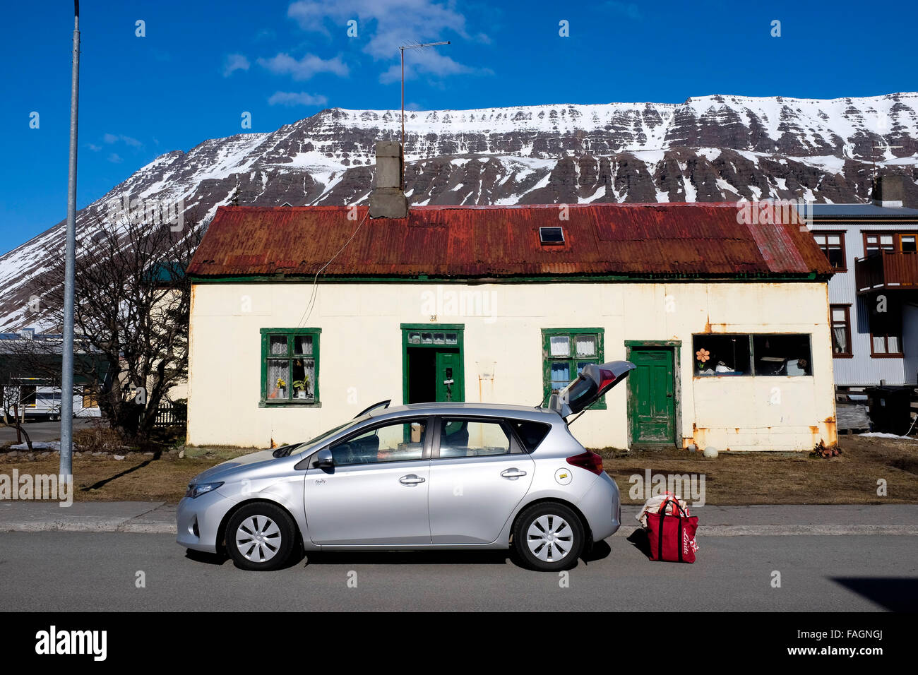 A rental car outside a house in Isafjordur against the dramatic hills and mountains behind in the westfjords of northern Iceland Stock Photo