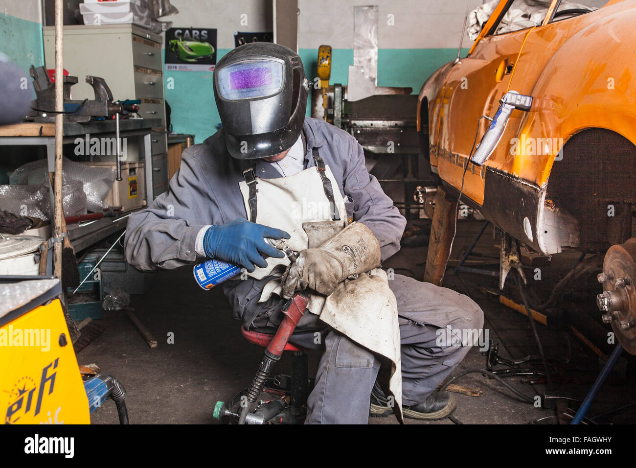 Coachbuilder restores a classic car VW Karmann Ghia. Welder cleans the welding equipment. Stock Photo